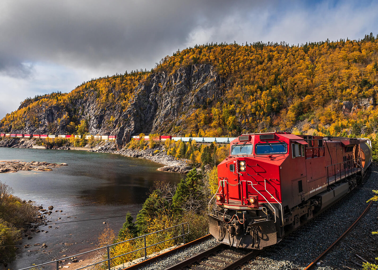 a red train rolling down the track along the shoreline